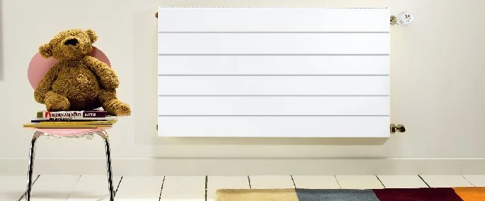 Radiador de panel instalado en una habitación junto a una silla — reparacioncalderas.madrid